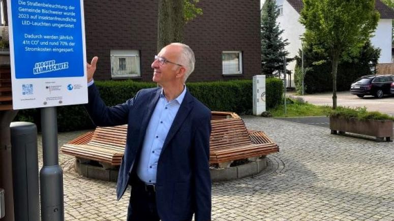 Herr Bürgermeister Wein zeigt auf das neue Klimaschutzschild vor dem Rathaus Bischweier        