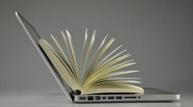 Laptop geöffnet mit einem aufgeschlagenen Buch darin