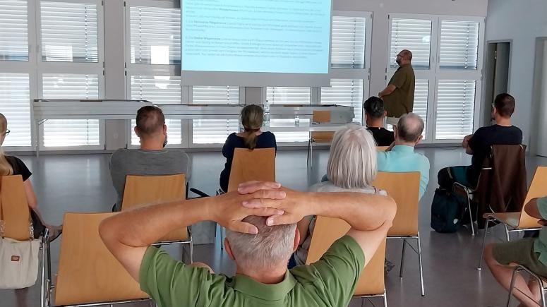 Stühle mit Menschen im Dorfhaus im Vortrag Schädlinge